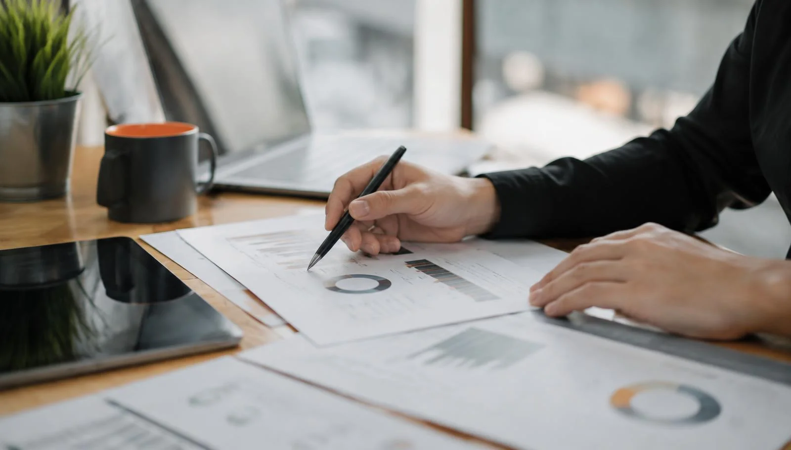 Hands reviewing printed marketing performance charts beside a tablet and laptop